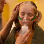 A woman assists a little girl with an inhaler, providing care and support for her respiratory needs