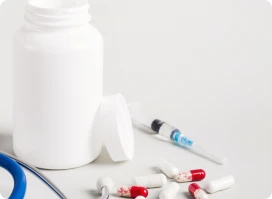 Still life of a pill bottle, loose capsules, a syringe, and a stethoscope.