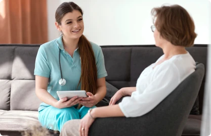 Female nurse smiling while talking to an older woman during a home visit.