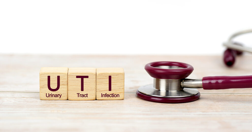 Close-up of wooden blocks spelling "UTI" with definitions below, beside a stethoscope on a light wooden surface.