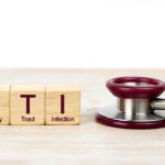 Close-up of wooden blocks spelling "UTI" with definitions below, beside a stethoscope on a light wooden surface.