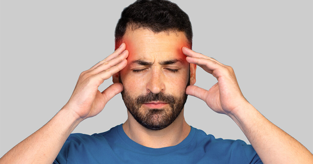 A man is holding his head in pain, indicating he is suffering from a headache.