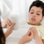 Child lying in bed with fever and possible dehydration while caregiver offers medicine and water for treatment