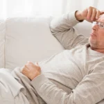 Older man feeling tired on the couch from cholesterol-related fatigue.