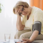 Older woman checking blood pressure at home while experiencing a headache.