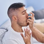 Person taking inhaler for immediate wheezing relief at home.